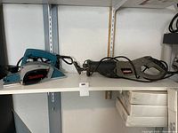 Makita power planer and Craftsman reciprocating saw placed side by side on a shelf.