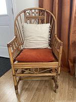 Front view of rattan armchair with white tassel pillow and burnt orange seat cushion