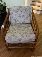Front view of the rattan chair showing the floral cushions and curved armrests.