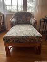 Front view of rattan chaise lounge chair with floral cushions showing full length and cushion pattern.