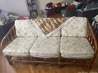 Front view of the rattan 3-seater couch with three floral cushions and a decorative throw partly draped over the couch.