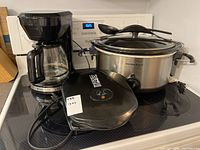 Three kitchen appliances on stove: a Hamilton Beach slow cooker, George Foreman grill, and Toastmaster coffee maker.