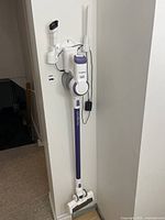 Full view of Tineco A10 Dash cordless stick vacuum mounted on wall charging dock with power cord connected and attachments in holders.
