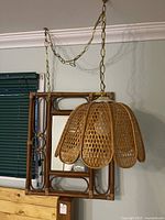 Photo of vintage rattan swag lamp and matching wall mirror hanging on wall. Lamp has flower petal shaped rattan shade and metal chain.