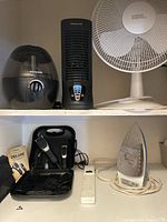 Full view showing Honeywell humidifier, Honeywell tower fan, Everyday Essentials pedestal fan, Wahl deluxe haircutting kit in case, power strip, and Beaumark iron on a shelf.