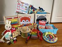 Full view of lot showing large fabric animal bins, colorful abacus, wooden xylophone, tambourine, handmade bunny, Sensory Bin, finger puppets, Cognitive Letters game, and various wooden instruments and toys scattered.