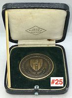 Bronze sports award medal in original presentation box, with dark green velvet base and cream silk-lined lid stamped 'John Pinches London'. The medal is sized approximately 1.5 inches in diameter.