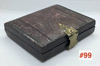 Closed dark leather-like antique photo case with brass latch, visible surface wear, square shaped.
