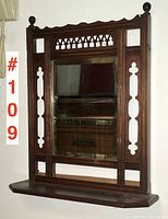 Full front view of antique walnut framed last look mirror with shelf mounted on wall.