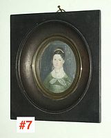 Rectangular dark wood frame with oval gilt inner mount displaying the portrait miniature of a woman in a green dress.