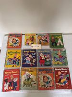 Photo showing 12 Howdy Doody Golden Books arranged in three rows on white surface. Covers vary in color with distinct, vintage illustrated art depicting Howdy Doody and related characters in circus and holiday themes.