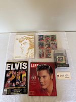 Top-down photo of Elvis Presley books, magazines, vintage cards, and boxed ornament arranged on a flat surface.