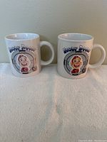 Two white ceramic mugs featuring cartoon Howdy Doody faces and text