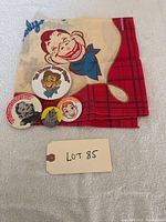 Photo showing the folded 1988 NBC Howdy Doody scarf with a large Howdy Doody character face and four collectible pins arranged alongside, all in excellent condition.