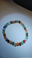 Natural mixed gemstone stretchy bracelet in round beads of multiple colors including blues, greens, oranges, blacks, and reds under white light against a white background.
