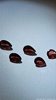 Five deep red pear cut garnet gemstones arranged in a line on a white surface.