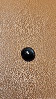 Close-up image of a round jet black gemstone cabochon on textured background, showing smooth surface and polished dome shape.