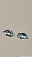 Two natural sky blue marquis cut topaz gemstones placed on a neutral surface, showing the facets and color clearly.