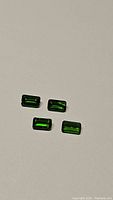 Four natural emerald cut chrome diopside gemstones arranged on a light background showing deep electric green color and bright facets.
