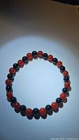 Photo showing a circular stretchy bracelet made of alternating black and red polished gemstone beads, approx. 6mm round beads.