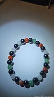 Image showing the full circular stretchy bracelet with alternating black, green, white, and red-orange beads on a plain background under spotlight.