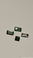 Four natural tourmalines, light and dark green color, rectangular and square cuts, arranged on neutral background.