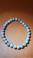 Photo of natural map jasper stretchy bracelet laid flat showing round beads with map-like patterns in shades of gray and black on light gray background.
