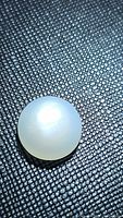 Close-up photo of a round white moonstone cabochon with visible flash on textured black surface.