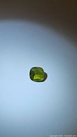 Photo of 2.14ct natural apple green peridot gemstone displaying cushion cut and natural inclusions under lighting.