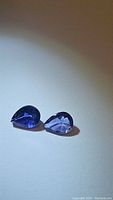 Two pear cut natural purple iolite gemstones on a light background, showing color and shape.