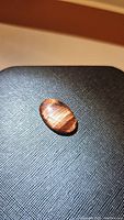 Oval cabochon cut natural red tiger's eye showing hologram-like flash and striations on a textured black background.