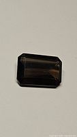 Natural smokey quartz emerald cut gemstone photographed on plain background in natural light to show details of cut and clarity.