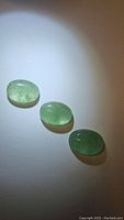 Three oval green strawberry quartz cabochons placed in a row on a white background with spotlight illumination.