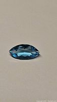 Marquise cut Natural Swiss Blue Topaz gemstone placed on a neutral surface, showing vibrant blue color and facet reflections, front view.