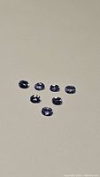 Seven oval cut purple-blue tanzanite gemstones displayed on a light surface, showing clarity and color.