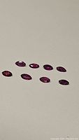 Photo showing 9 marquis cut rubies in deep red-pink-purple colors arranged on a flat surface.