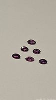Six fushia purple faceted sapphires arranged in a scattered triangle on a plain surface.