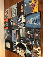 Photo showing approximately 20 1980s vinyl LP albums arranged side by side on floor, covers including classic rock, pop, and new wave bands.