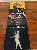 Four LP record covers stacked, showing three Steve Martin comedy albums and one Bill Cosby album in good condition.