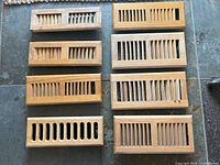 8 wooden heat vent registers displayed on floor with varying slat widths and designs
