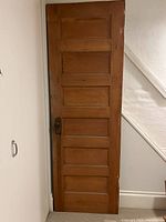Solid wood door standing upright against a wall, showing the full front exterior surface with metal door knob and recessed panels.