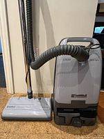 Side view of Kenmore canister vacuum cleaner showing the hose connected to the main unit and floor head on a carpet floor.