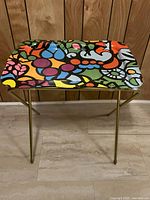 Multi-coloured abstract patterned TV tray with vibrant colors and gold-tone folding legs.