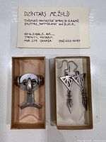 Business card of artist and both brooch and earrings displayed in wooden boxes