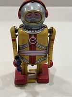 Front view of vintage yellow and red wind-up space robot toy holding a blue gun with printed space suit details.