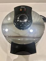 Exterior view of Oster waffle maker showing shiny chrome lid with black control section and handle