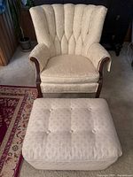Front view of white antique style easy chair with shell back and wooden armrests paired with matching ottoman.