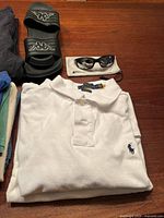 Folded Polo Ralph Lauren white polo shirt with sunglasses and slides