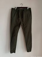 Front view of green men's track pants showing elastic waistband, drawstring, and tapered cuffs