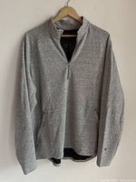 Full front view of light grey men's half zip sweater hanging on wooden hanger showing zipper, collar, and pocket openings.
